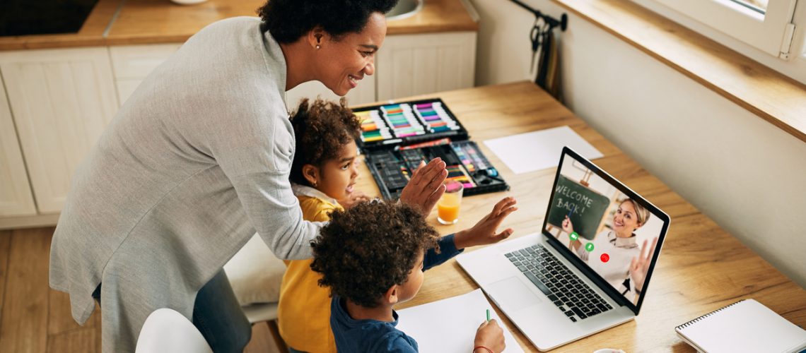Happy black mother and kids waving to a teacher while having video call over a computer from home.