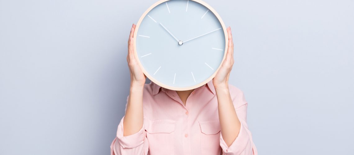 It's 10:10 o'clock. Portrait of charming pretty positive cheerful woman closing covering head face with round clock isolated on grey background