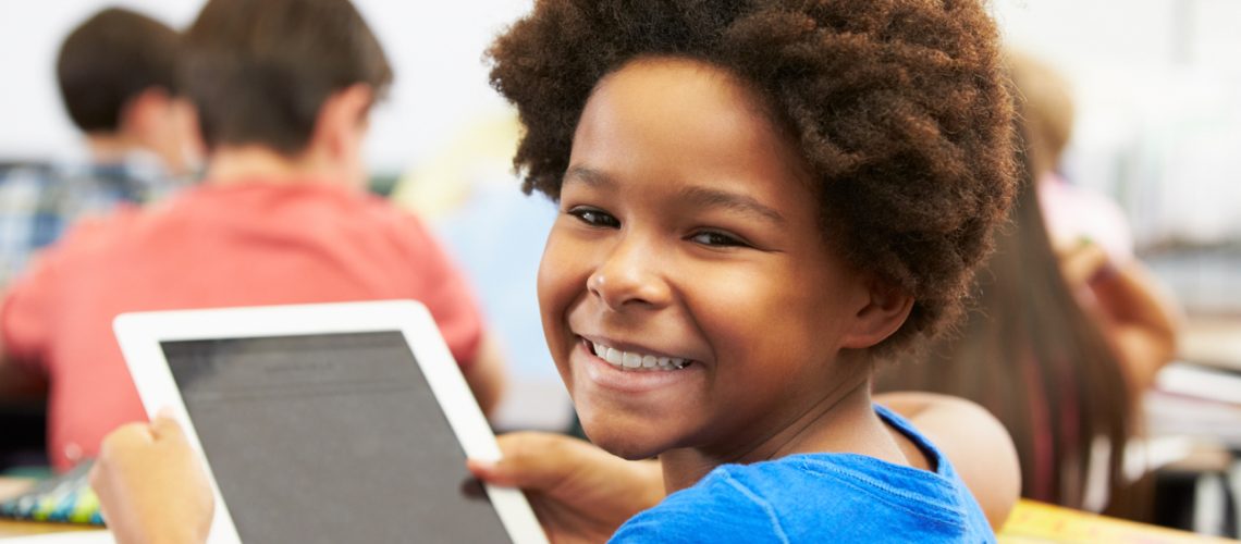 Pupil In Class Using Digital Tablet Looking To Camera Smiling