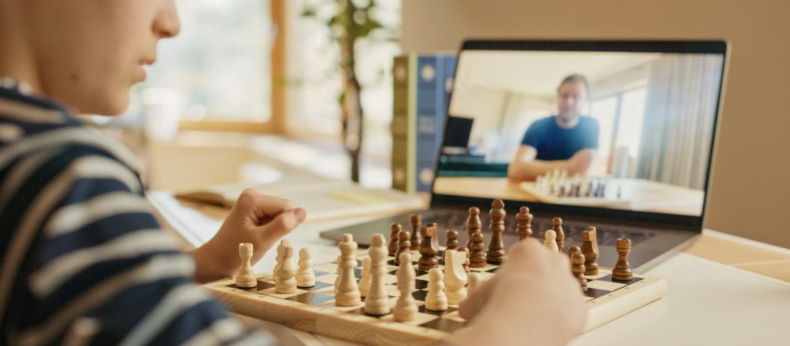 Brilliant Little Boy Playing Chess with His Distant Relative or Uncle, Uses Laptop for Video Call. Remote Online Education, E-Education, Communication with Family, Homeschooling.